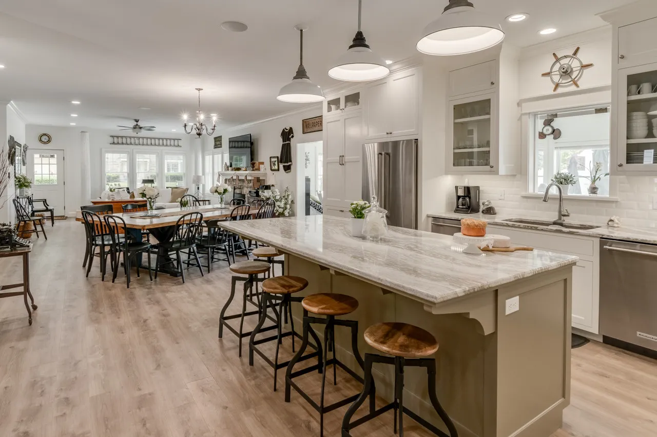Open lake house kitchen with a long Cambria island, bar stools and a dining table beyond