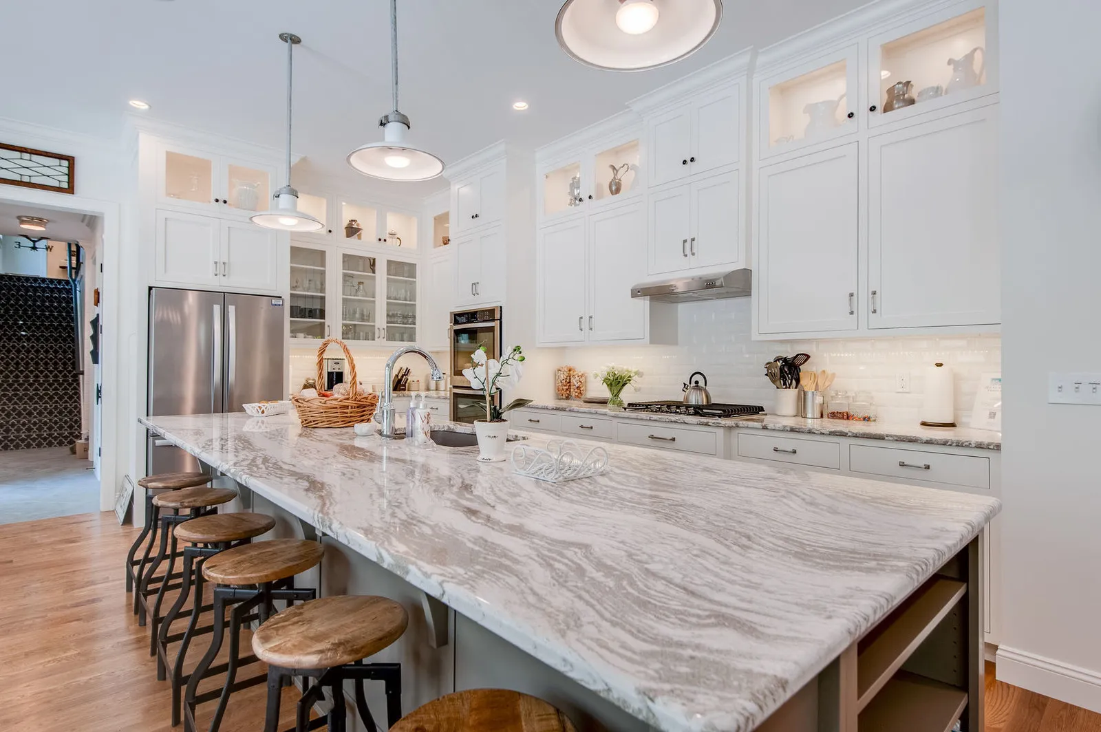Long kitchen island topped in grey and white Cambria Oakmoor quartz with a row of bar stools, white cabinetry behind