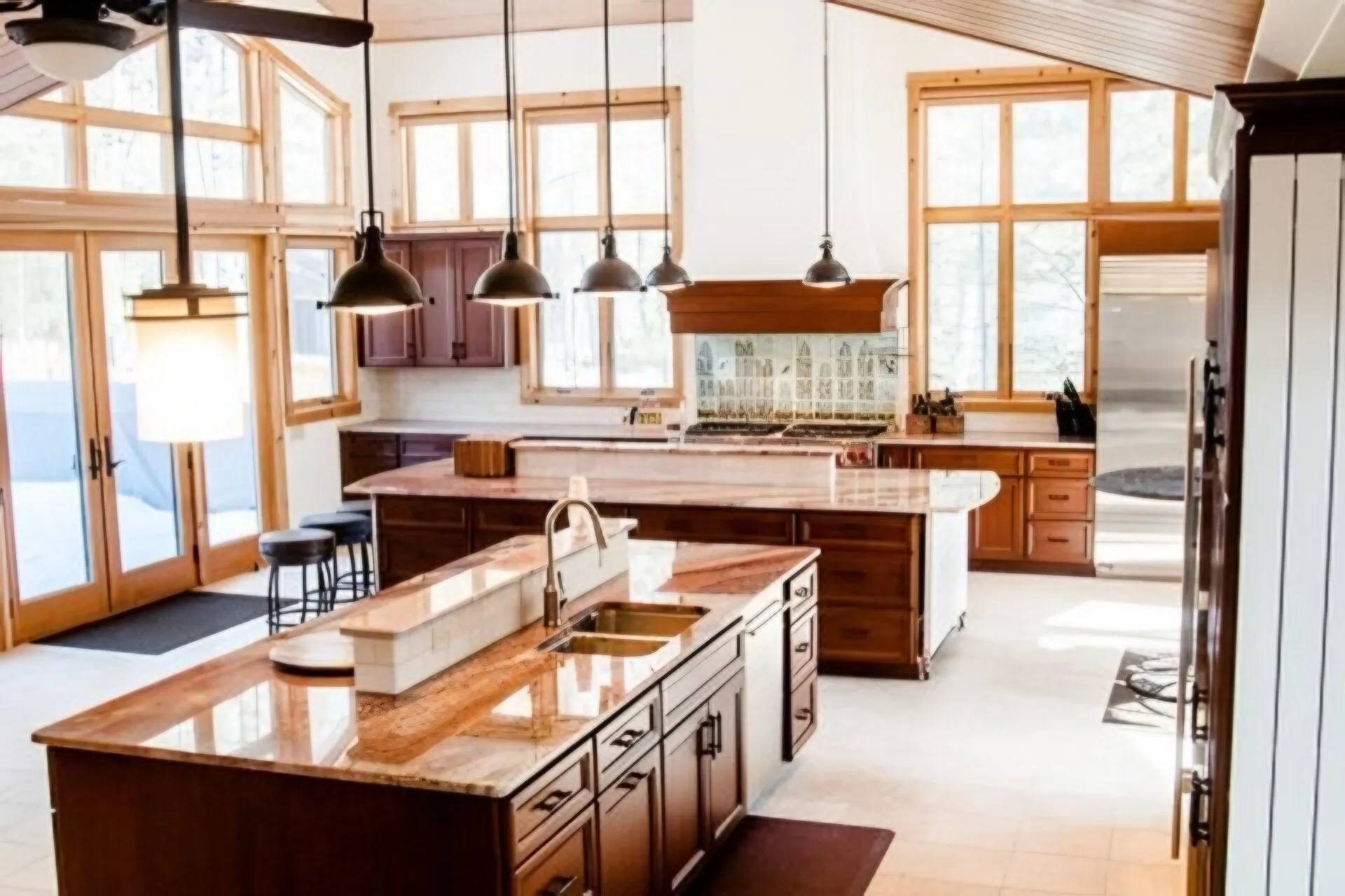Bright cottage kitchen with two stone-topped islands, dark stained cabinets and black pendant lights under a pine ceiling