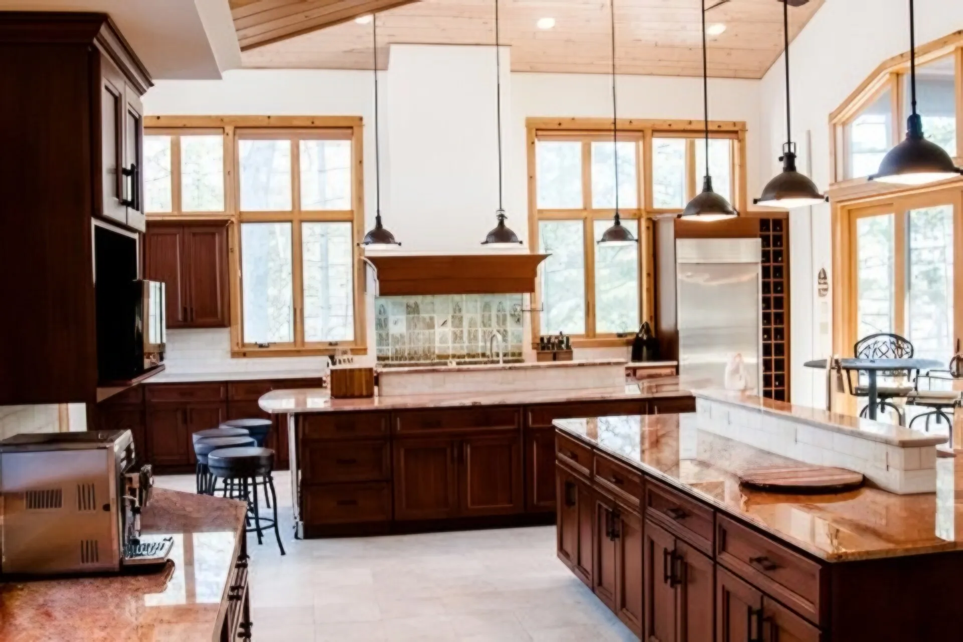 Large cottage kitchen with stained wood cabinetry, two polished stone islands and tall wood-framed windows